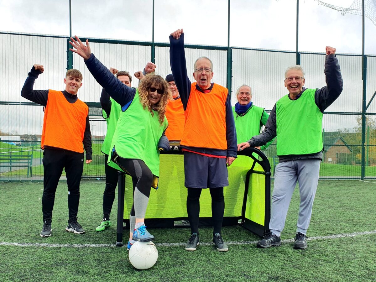 a group of women and men celebrating in a group photo after they've played walking football