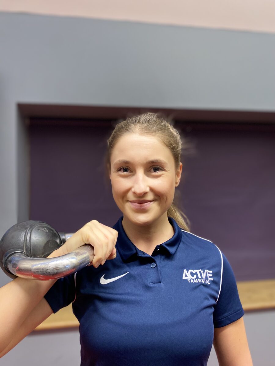 woman smiling, holding kettlebell at shoulder